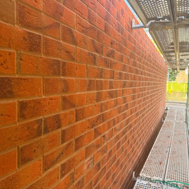 Long red facing brick elevation with straight courses and clean joints, seen from the scaffold on a large housing development